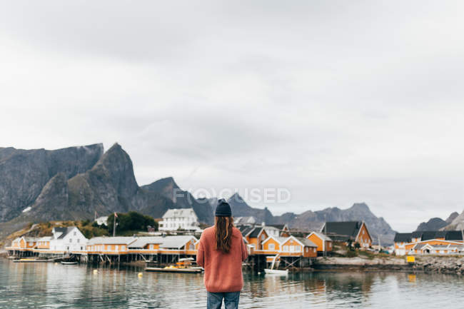 Vista posteriore della donna al lago con edifici rurali sulla riva opposta — Foto stock