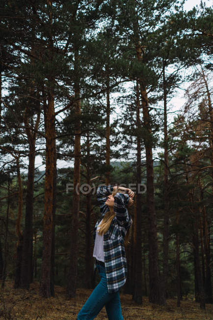 Vista laterale della ragazza bruna in camicia a scacchi che cammina nella foresta e alza lo sguardo . — Foto stock