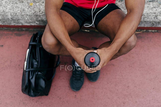 Cultivo hombre deportivo sentado cerca del bolso con la botella de deporte en las manos - foto de stock