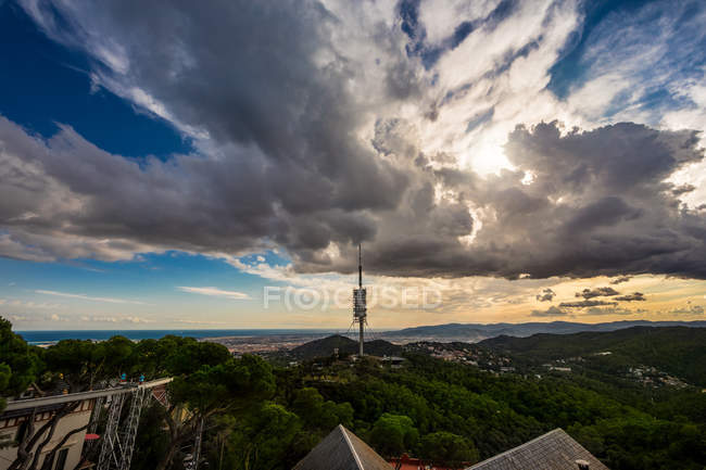Vista lejana de la torre de comunicación sobre árboles verdes y paisaje nuboso escénico - foto de stock