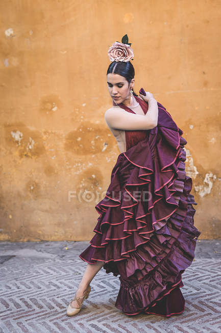 Танцовщица фламенко в типичном длинном костюме юбки, позирующая над стеной улицы на заднем плане — стоковое фото