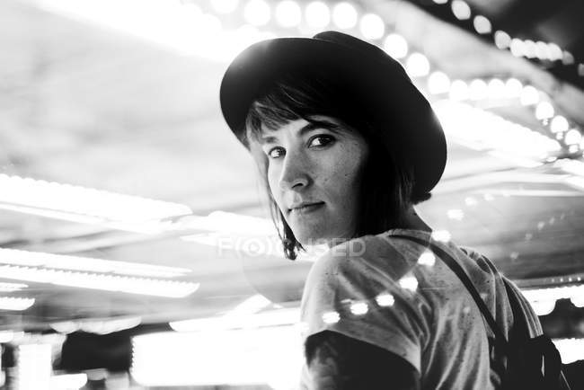 Porträt einer brünetten Frau mit Hut, die im beleuchteten Nachtpark über die Schulter in die Kamera blickt — Stockfoto