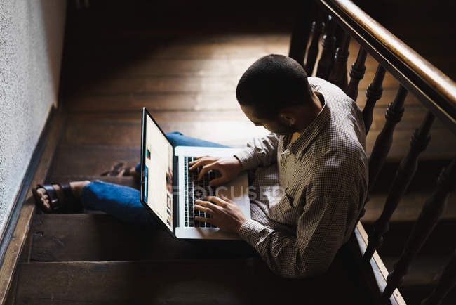 Низький кут зору чоловіка в картатій сорочці, що сидить на сходах і використовує ноутбук . — стокове фото