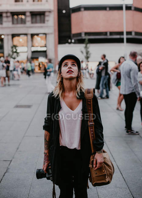 Frau mit Kamera in der Hand steht auf der Straße und schaut auf — Stockfoto