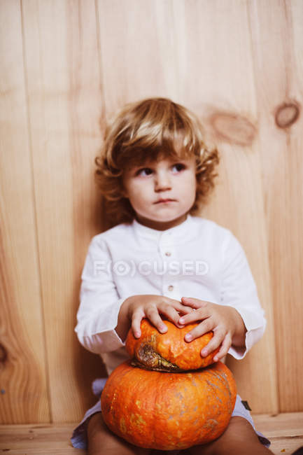 Adorable boy posing with pumpkin by wooden wall and looking away — Stock Photo