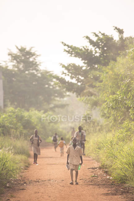 BENIN, ÁFRICA - 31 de agosto de 2017: La gente que camina por la carretera rural y mira a la cámara - foto de stock
