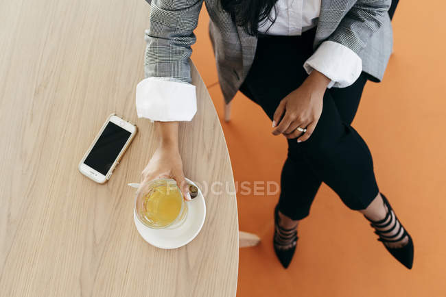 Erntebild von Frauenhänden, die eine Tasse Tee mit Smartphone auf dem Tisch halten — Stockfoto