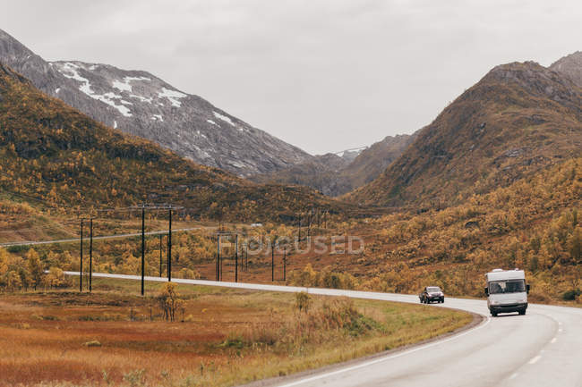 View to cars driving through mountains on asphalt road in cloudy day. — Stock Photo