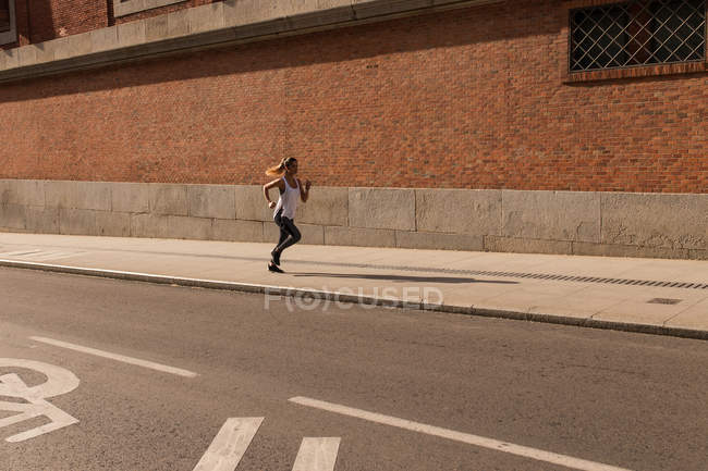 Mujer deportiva corriendo en el lado del paseo soleado - foto de stock