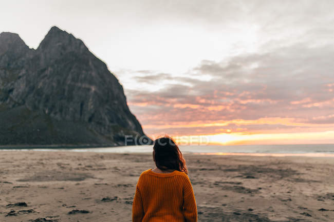 Vista trasera de la mujer disfrutando del amanecer en la playa de arena - foto de stock