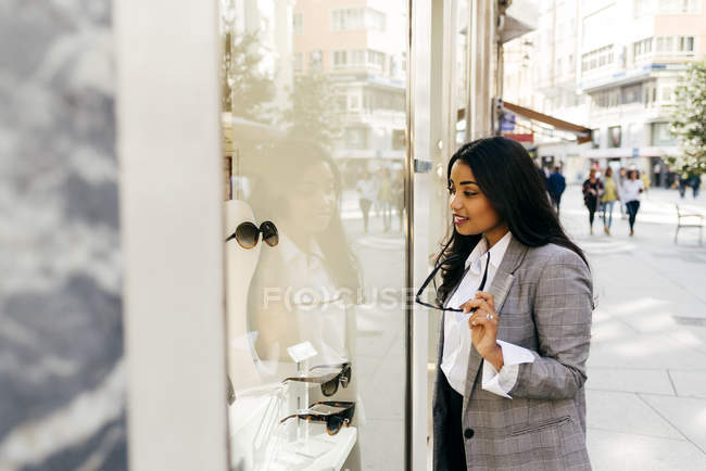 Mulher elegante com óculos olhando com interesse na vitrine da loja — Fotografia de Stock