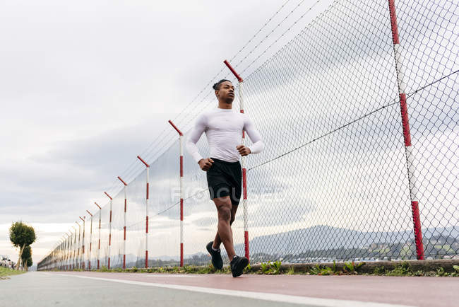 Low angle view of man in sportswear jogging on race track and looking forward . — Stock Photo