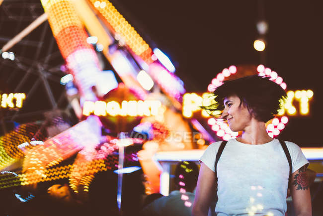 Jovem mulher balançando o cabelo feliz no fundo de luzes brilhantes do parque de diversões à noite . — Fotografia de Stock