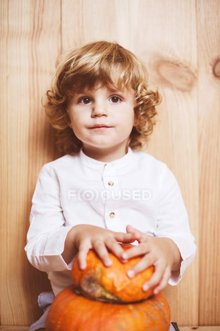 Enfant blond posant avec citrouille par un mur en bois — Photo de stock
