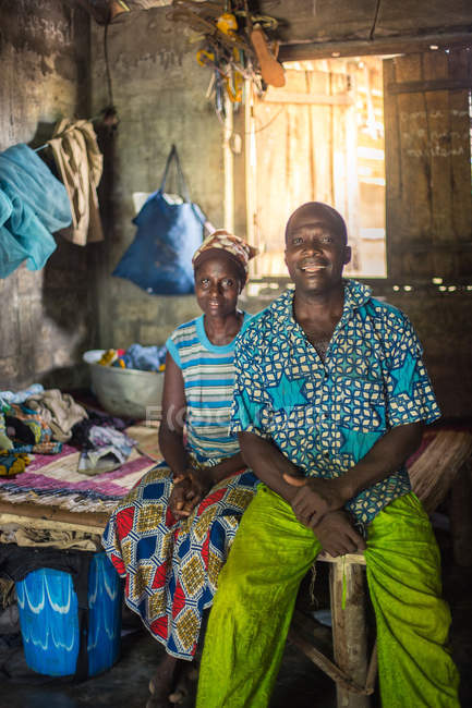 BENIN, ÁFRICA - 31 DE AGOSTO DE 2017: Homem e mulher negro alegre com roupas étnicas sentados em casa . — Fotografia de Stock