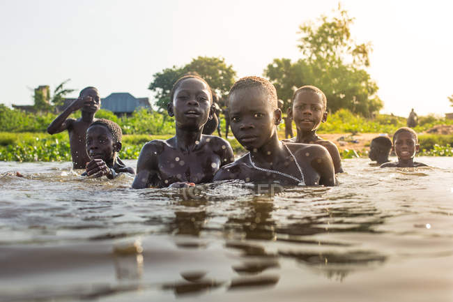 Бенин, Африка - 31 августа 2017 года: Группа детей, плавающих в реке и смотрящих в камеру на тропическом фоне . — стоковое фото