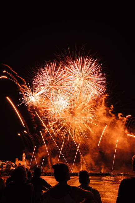 Silhuetas de pessoas admirando fogos de artifício salpicos no céu noturno — Fotografia de Stock