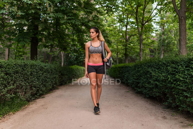 Sportswoman with backpack walking on park alley — Stock Photo