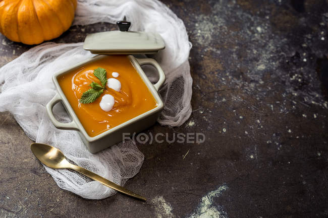 Low angle view of homemade cream of pumpkin in square ceramic bowl on white gaze with spoon — Stock Photo