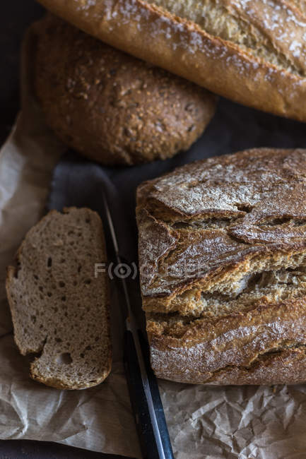 Vista superior de loafs de pão caseiros e fatias com faca na mesa rústica — Fotografia de Stock