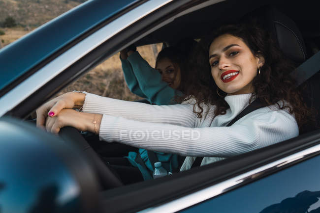 Усміхнена жінка за кермом машини і дивиться на камеру з другом, сидячи поруч . — стокове фото