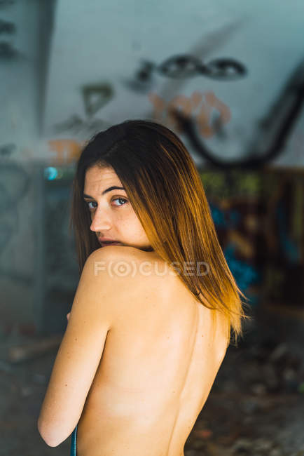 Donna in topless che guarda oltre la spalla la macchina fotografica in un edificio abbandonato — Foto stock
