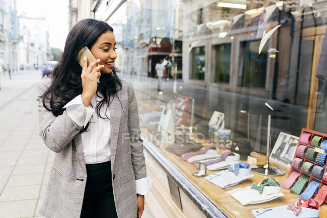 Retrato de mulher elegante olhando para a janela da loja ao ter uma conversa por telefone — Fotografia de Stock