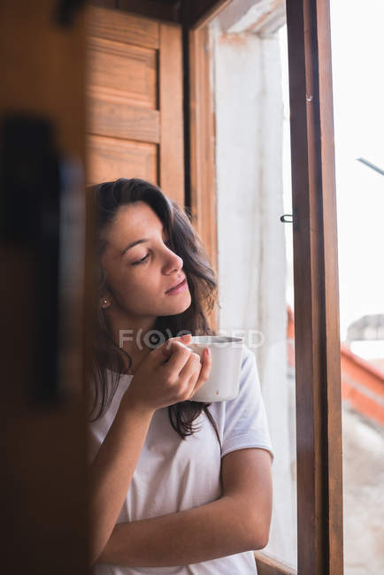 Mujer soñadora sosteniendo taza y mirando a la ventana . - foto de stock