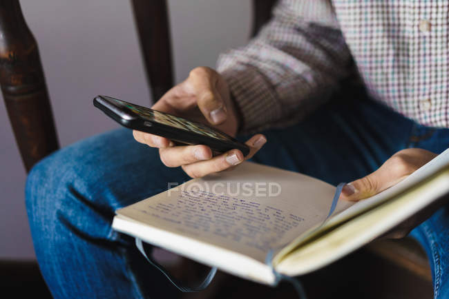 Crop man with notebook in hand and browsing smartphone — Stock Photo