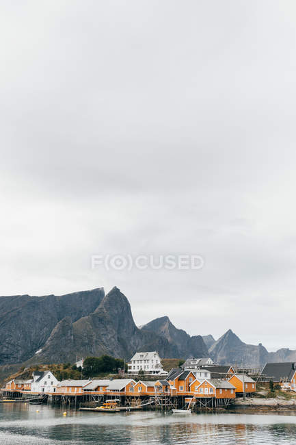Small mountain village on shore of lake on background of mountain peaks and cloudy sky. — Stock Photo