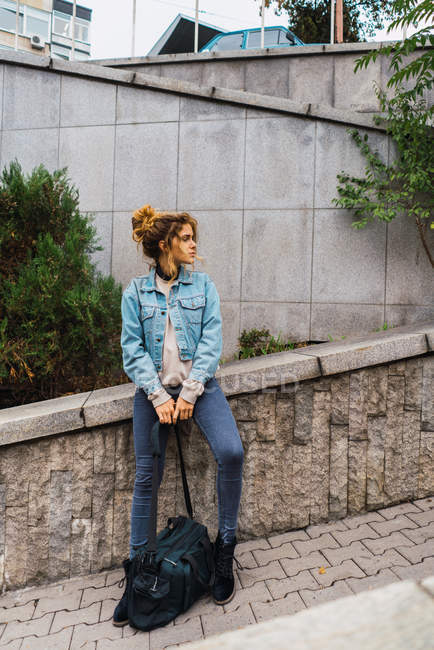 Selbstbewusstes Mädchen mit Reisehandtasche, an Zaun gelehnt und zur Seite schauend — Stockfoto