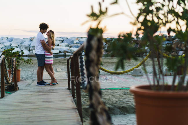 Vista lateral de abrazar a la pareja posando en el paseo marítimo - foto de stock