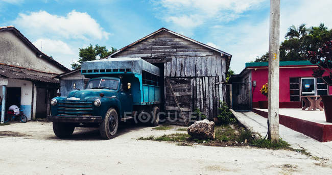 CUBA - AUGUST 27, 2016: Blue old truck parked under roof of wooden weathered garage at street. — Stock Photo