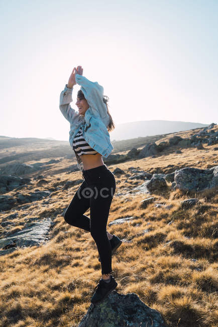 Vue latérale de la fille brune équilibrant sur la pierre au champ de campagne — Photo de stock