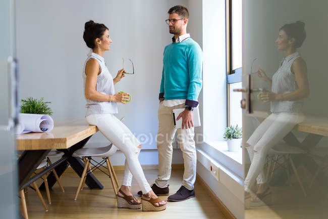 Side view of business people standing by window in modern office and talking — Stock Photo