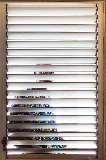 BENIN, AFRICA - AUGUST 31, 2017: Portrait of man standing behind window blinds and looking at camera. — Stock Photo