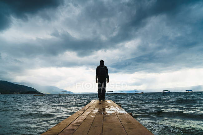 Vue arrière de l'homme posant sur une jetée au-dessus d'un ciel orageux — Photo de stock