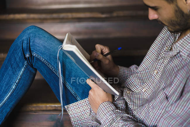 Vista lateral do homem sentado na escada e escrevendo no caderno — Fotografia de Stock