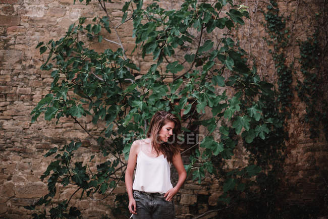 Porträt einer brünetten Frau, die an einer von Efeu umgebenen Mauer posiert und nach unten schaut — Stockfoto