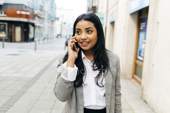 Елегантна бізнес-леді з телефоном, що йде по вулиці — стокове фото