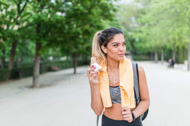 Усміхнена спортивна дівчина гуляє в парку і їсть закуску після тренування — стокове фото