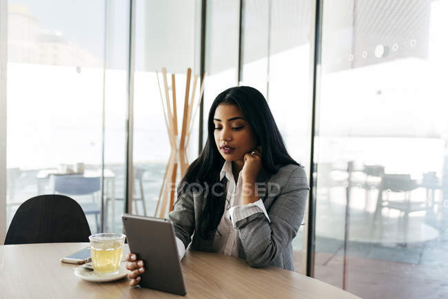 Portrait of businesswoman sitting at table and looking at tablet in hand — Stock Photo