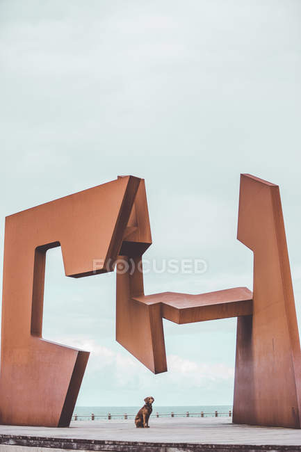 Собака сидит на площади со скульптурой современного искусства — стоковое фото