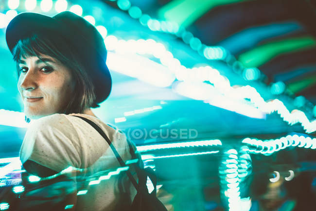 Стильная женщина смотрит через плечо на камеру в освещенном ночном парке — стоковое фото