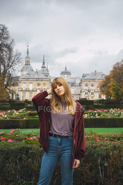 Brunette girl in casual clothes posing over mansion facade and garden on background — Stock Photo