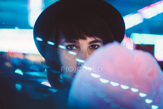 Стильна жінка в капелюсі покриває обличчя цукровою хмарою і дивиться на камеру — стокове фото