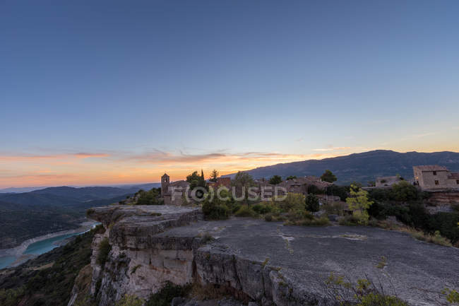 Vista à distância da aldeia no topo da montanha plana no fundo do vale ao pôr do sol — Fotografia de Stock