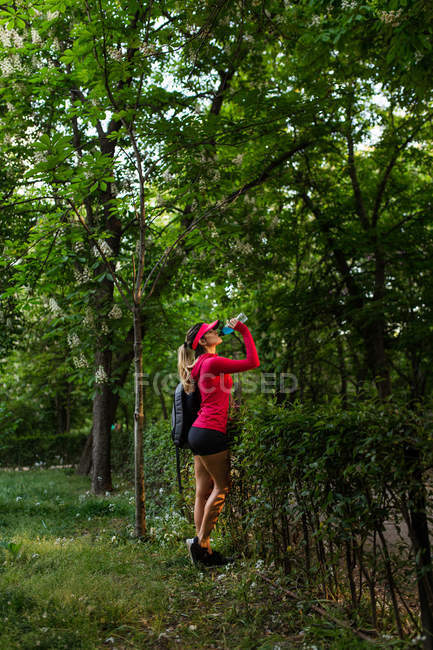 Side view of sportswoman drinking water after workout woods in park — Stock Photo