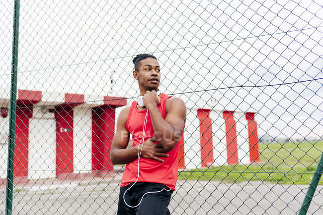Retrato de atleta con auriculares sobre hombros apoyados en valla y mirando hacia otro lado - foto de stock