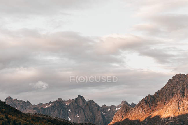 Paisagem de picos altos iluminados pelo sol sobre o céu nublado — Fotografia de Stock